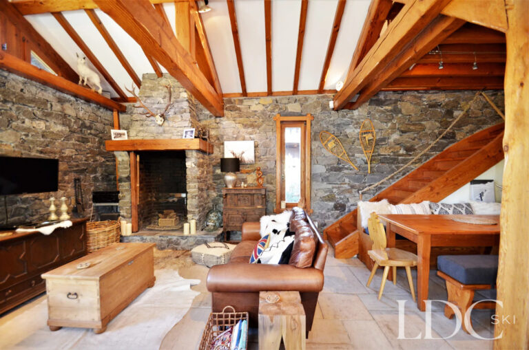 Lounge at Chalet Malina with stone fireplace, exposed timber beams and adjoining dining area