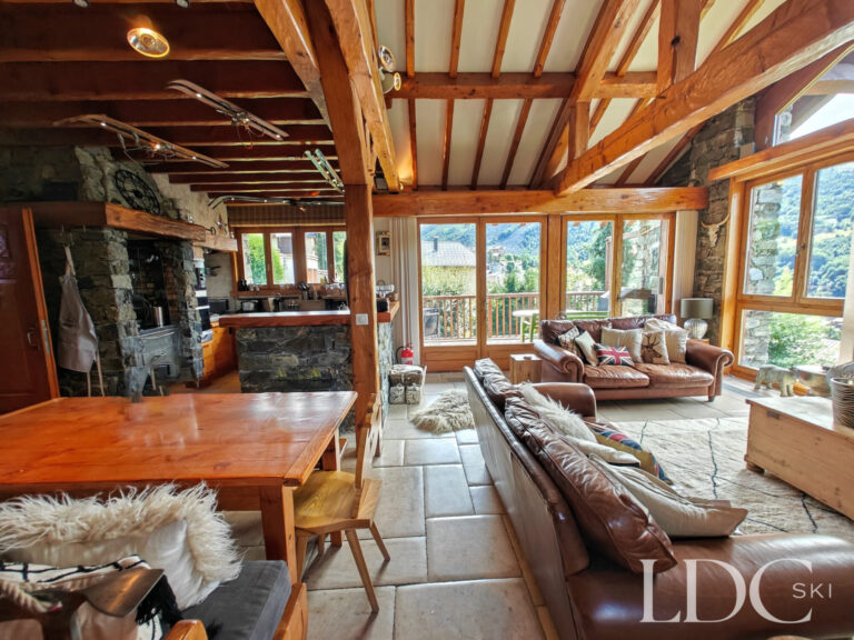 Open-plan living and dining area at Chalet Malina with exposed beams and windows overlooking the mountains