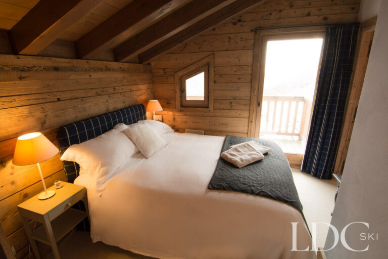 Double bedroom at Chalet Riondaz with timber walls and doors opening onto a balcony