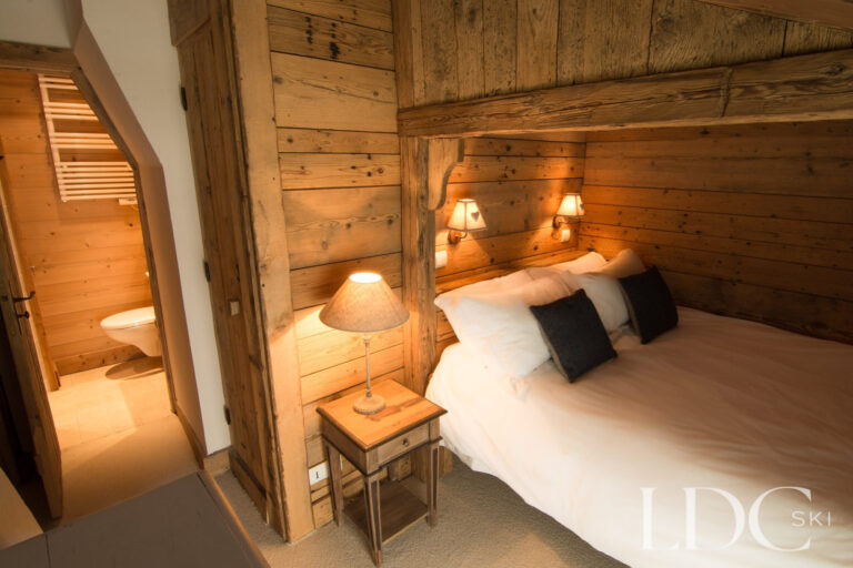 Double bedroom at Chalet Riondaz with timber walls and adjoining en-suite bathroom
