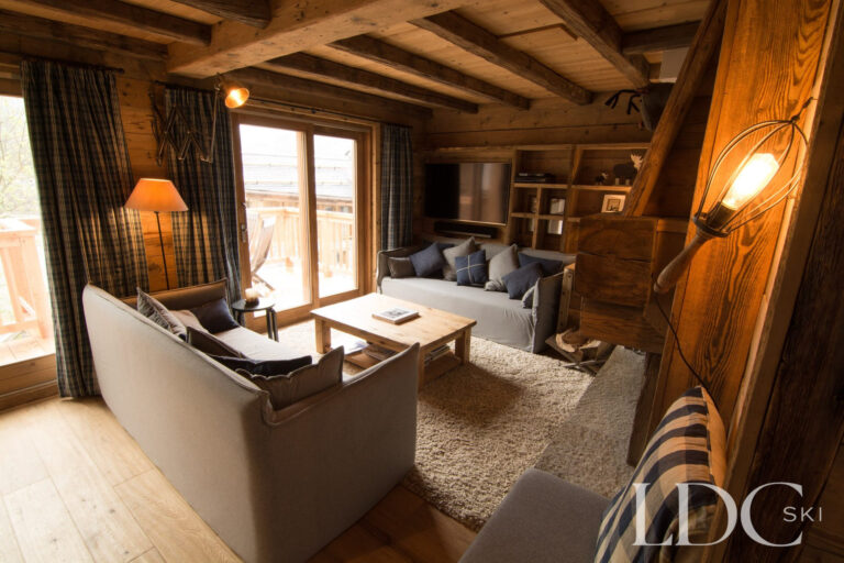 Comfortable lounge at Chalet Riondaz with sofas, exposed beams and doors opening onto the balcony