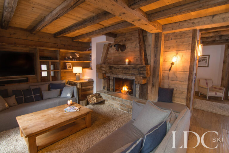 Traditional lounge at Chalet Riondaz with sofas, timber beams and open fire in a stone fireplace