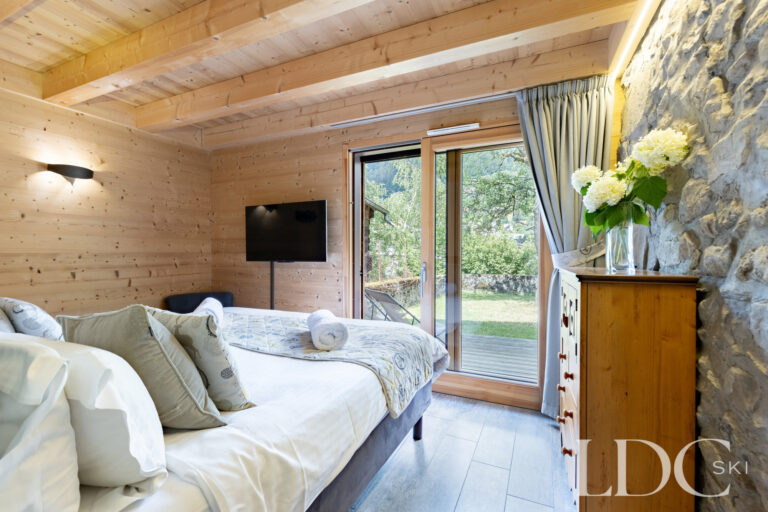 Twin bedroom with timber walls and doors opening to the garden at La Ferme de la Couttetaz