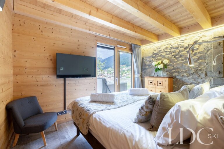 Double bedroom with timber feature wall and doors opening outside at La Ferme de la Couttetaz