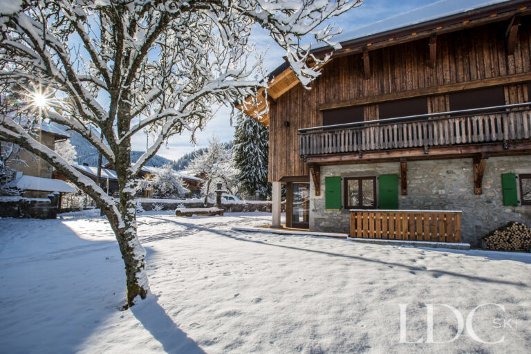 Snow-covered garden and traditional exterior of La Ferme de la Couttetaz in Morzine