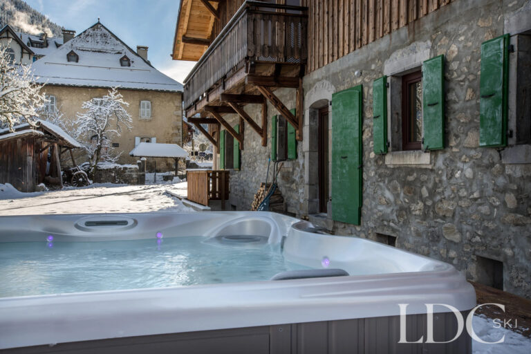 Outdoor hot tub beside the traditional stone exterior of La Ferme de la Couttetaz