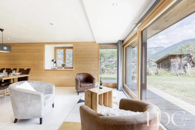 Bright lounge with floor-to-ceiling windows overlooking the garden at La Ferme de la Couttetaz