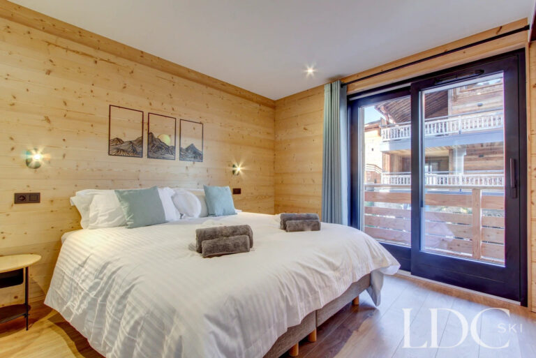 Double bedroom with balcony doors and timber walls at Piste Bleue
