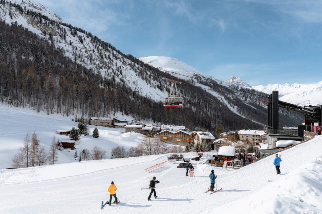Skiers on the slopes above Val d'Isère with the village and mountains beyond. © Yann Allègre
