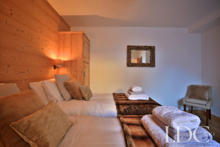 Warmly furnished double bedroom with wood-panelled wall at Chalet Aphylla
