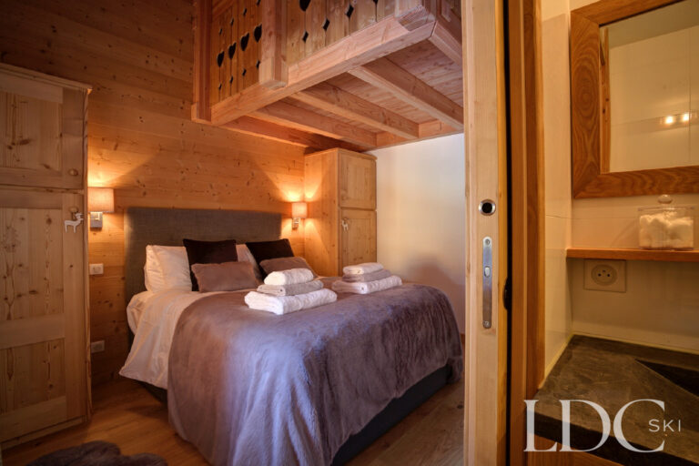 Double bedroom with exposed timber and adjoining bathroom at Chalet Aphylla