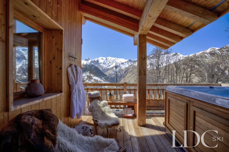 Covered terrace with private hot tub and seating overlooking the mountains at Chalet Aphylla