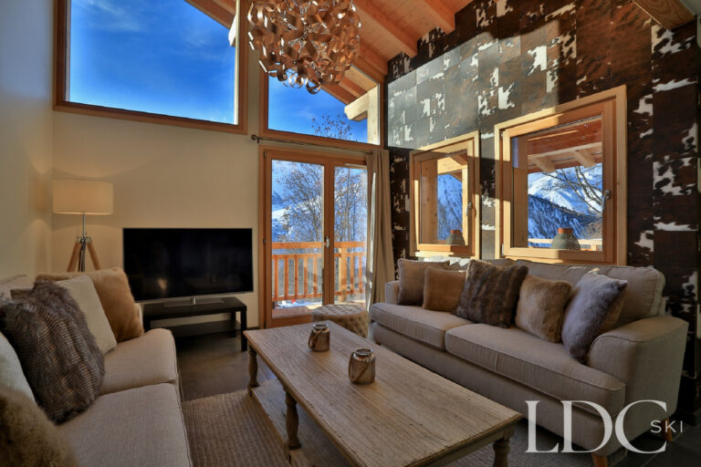 Contemporary alpine living room with fireplace and large mountain-facing windows at Chalet Aphylla