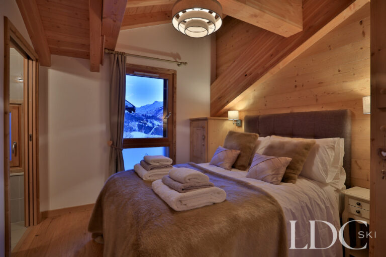 Double bedroom with warm timber interior and evening mountain view at Chalet Aralia