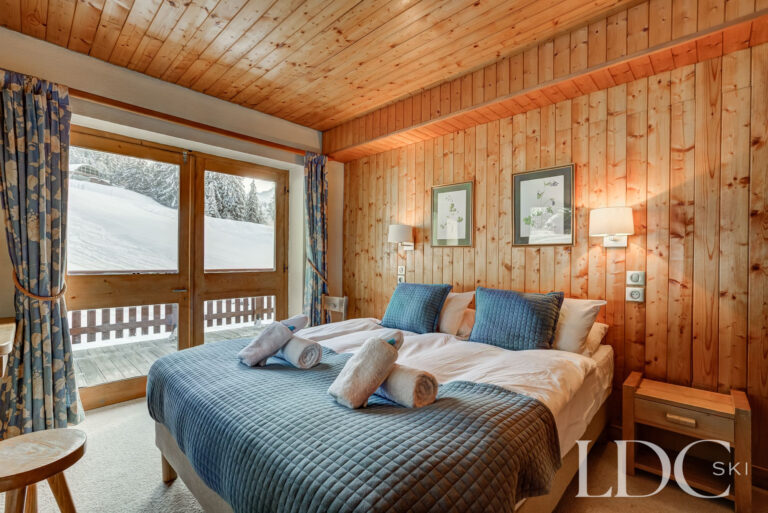 Double bedroom with timber-panelled walls and balcony access at Chalet Cecilia in Méribel
