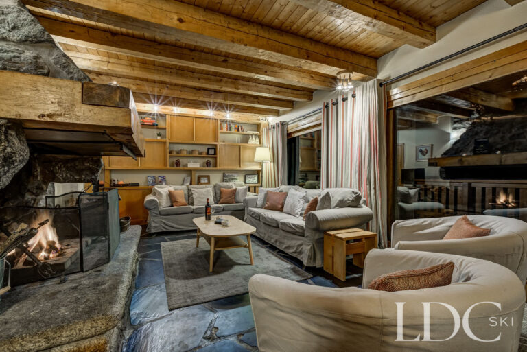 Cosy lounge with sofas, exposed timber beams and roaring log fire at Chalet Cecilia