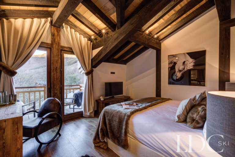 Master bedroom with vaulted timber ceiling and balcony access at Chalet Chez Bugi