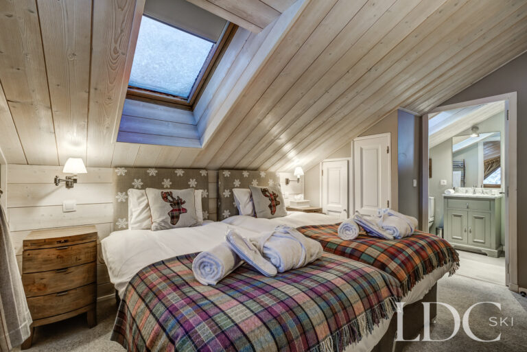 Double bedroom with sloping timber ceiling and en-suite bathroom at Chalet Pasarale in Méribel