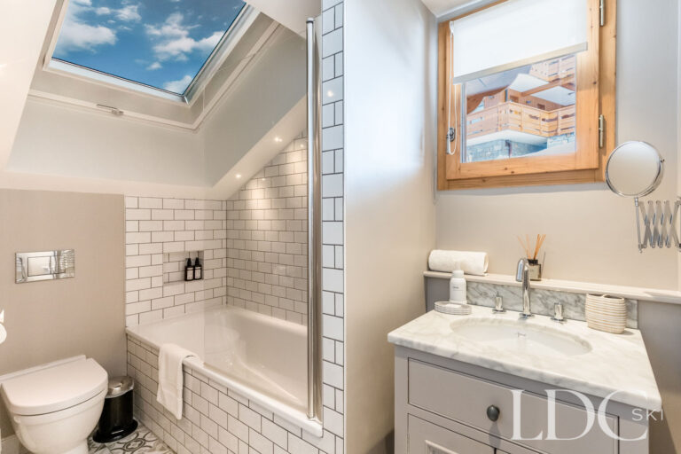 Bright en-suite bathroom with bath beneath a roof window at Chalet Quatre Meules