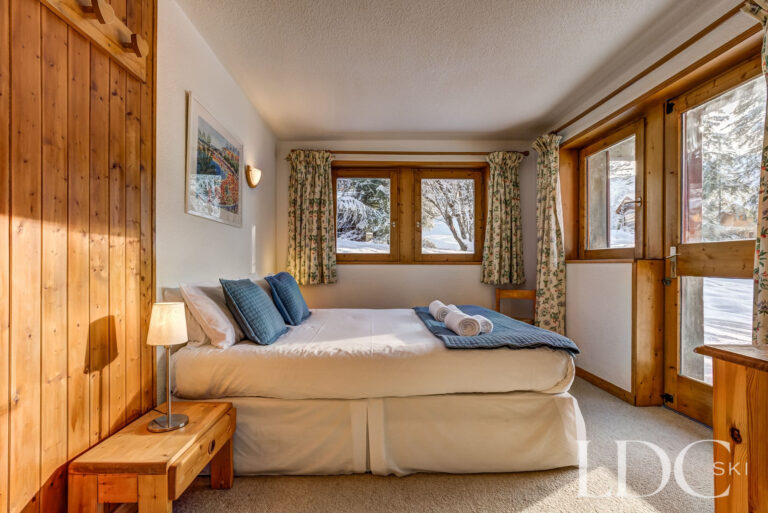 Double bedroom with wood panelling and windows overlooking the snow at Chalet Veronica