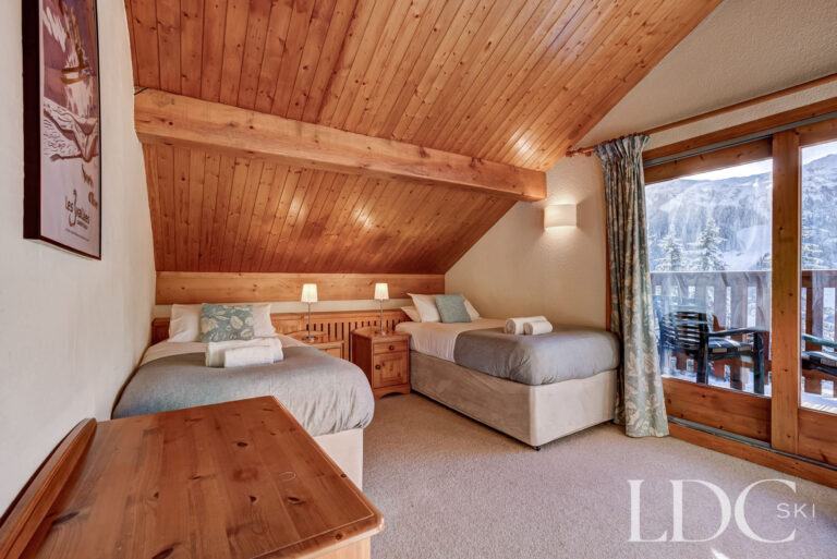 Twin bedroom beneath exposed timber beams with balcony access at Chalet Veronica