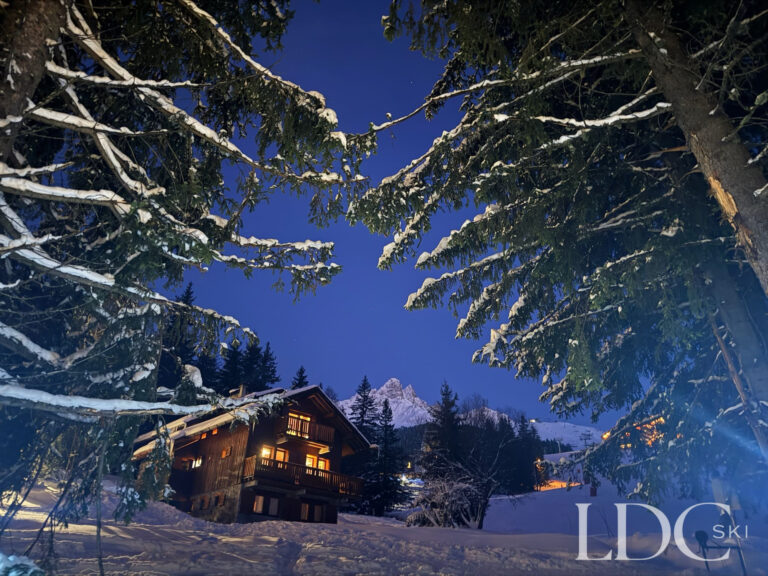 Chalet Veronica illuminated at dusk among snow-covered trees in Méribel