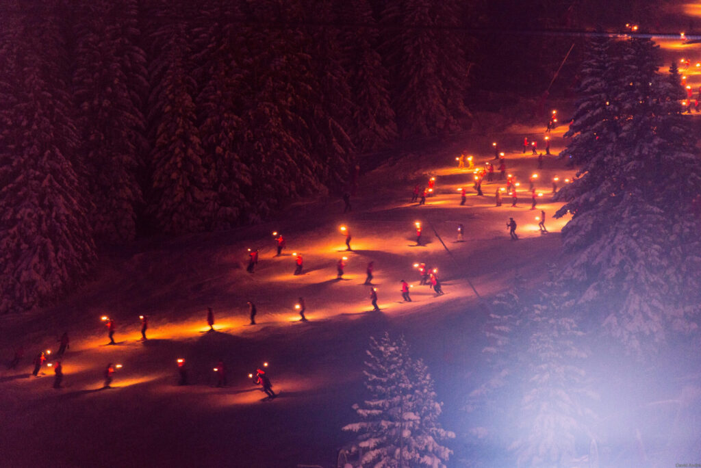 Torchlight ski descent illuminating the snowy slopes of Courchevel 1850 at night. © David André