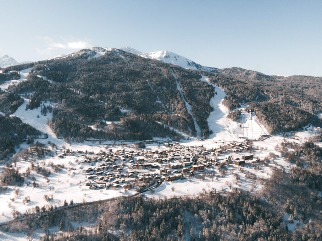 Aerial winter view of Courchevel Le Praz surrounded by forest and snowy slopes. © Un Duo.