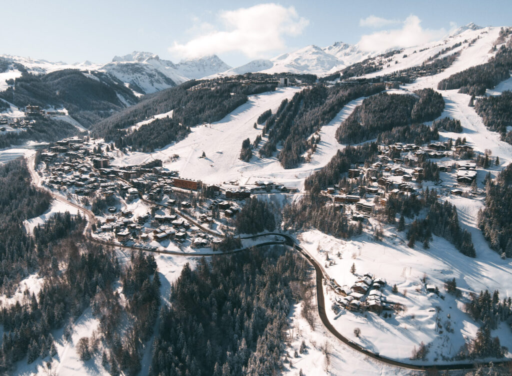 Aerial winter view of Courchevel Village surrounded by snowy slopes and forest. © Un Duo.