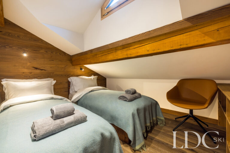 Blue bedroom arranged with twin beds beneath the sloping timber ceiling at La Florette