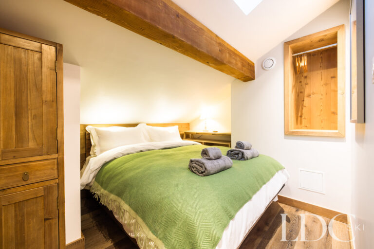 Double bedroom with green bedspread and exposed timber beam at La Florette