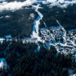 Aerial winter view of La Tania village surrounded by forest with ski slopes descending towards the resort. © Courchevel Tourisme