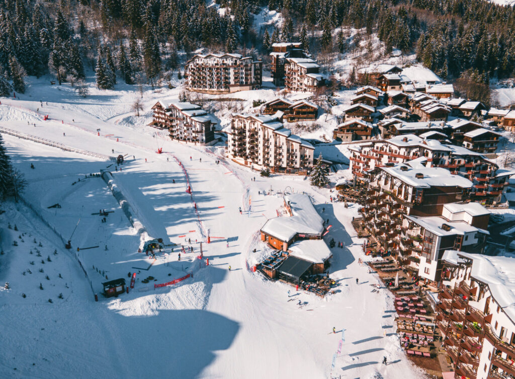 Aerial winter view of La Tania village and snow front surrounded by snowy forest. © Un Duo.