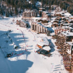 Aerial winter view of La Tania village and snow front surrounded by snowy forest. © Un Duo.
