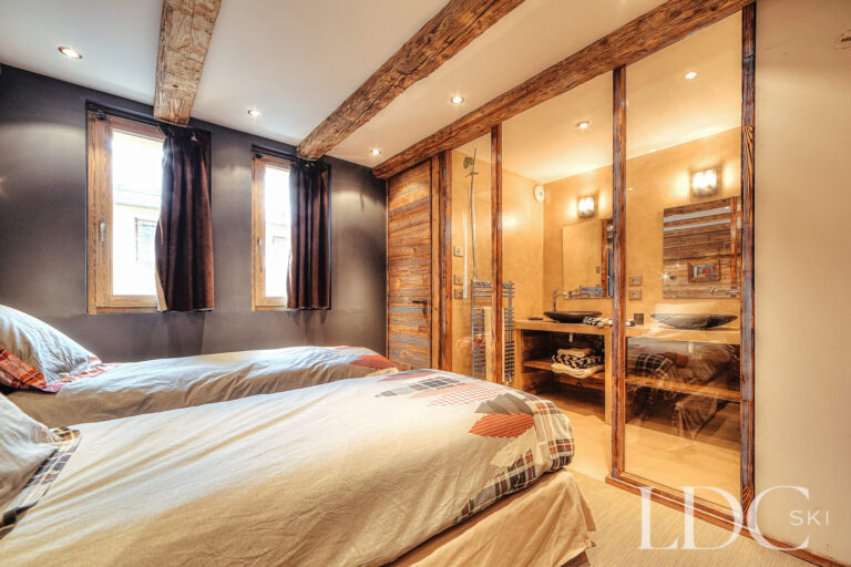 Twin bedroom with en-suite bathroom and exposed wooden beams at Le Chalet