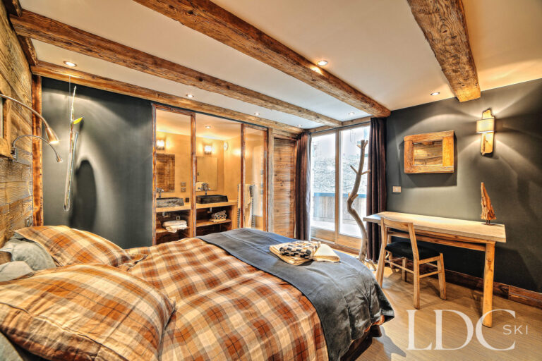 Double bedroom with exposed beams and a small seating area at Le Chalet