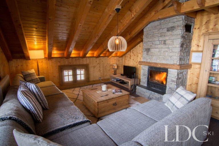 Cosy lounge with stone fireplace and exposed timber beams at Perce Neige in St Martin de Belleville