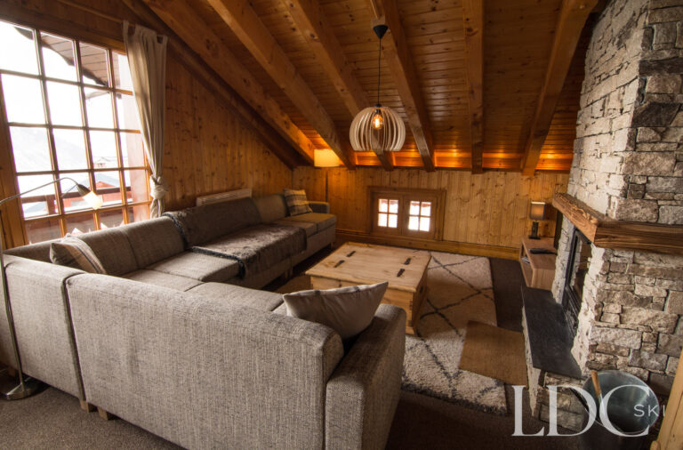 Spacious timber-lined lounge with stone fireplace at Perce Neige in St Martin de Belleville