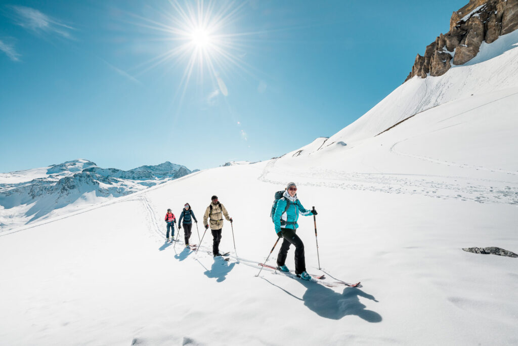 Ski tourers crossing the high mountain landscape beneath blue skies in Tignes. © Andy Parant