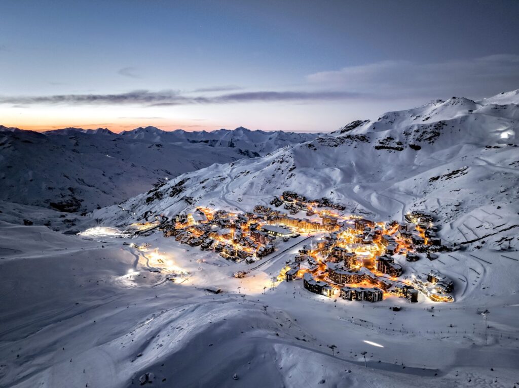 Aerial view of Val Thorens glowing beneath the mountains at dusk. © J. Carret – OT Val Thorens
